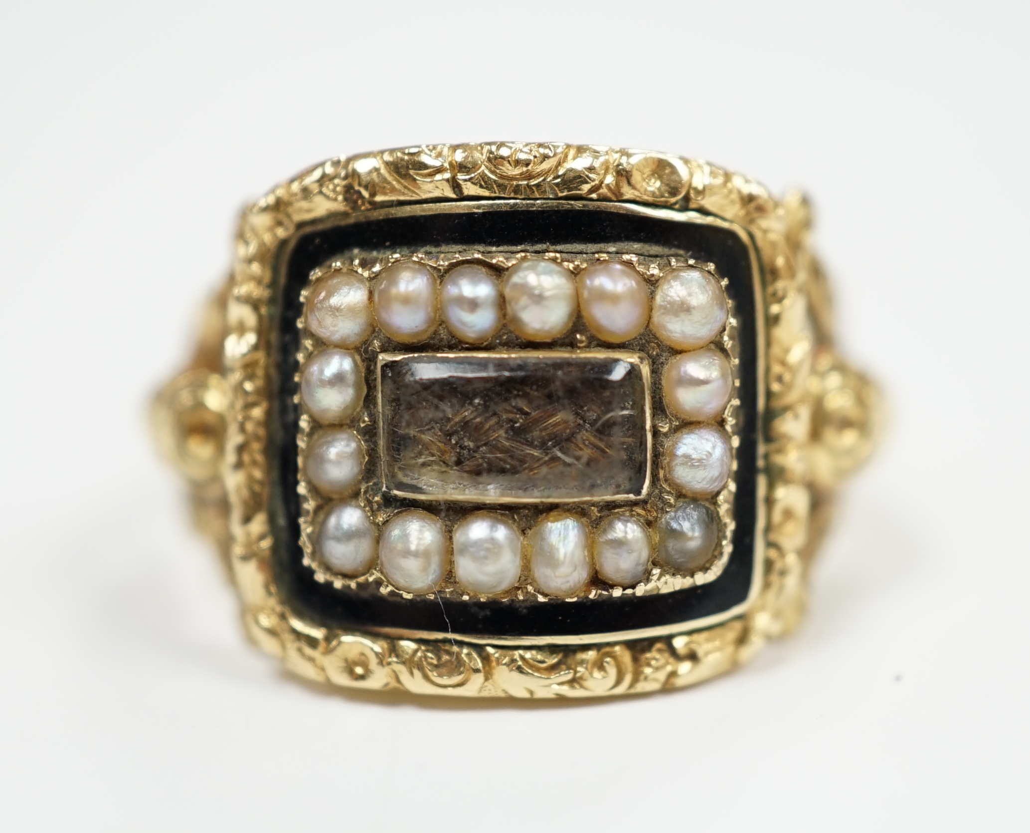 A George IV 18ct gold, black enamel and seed pearl set mourning ring, with plaited hair beneath a glazed panel, size Q, gross weight 5.6 grams, hallmarked for London, 1829.